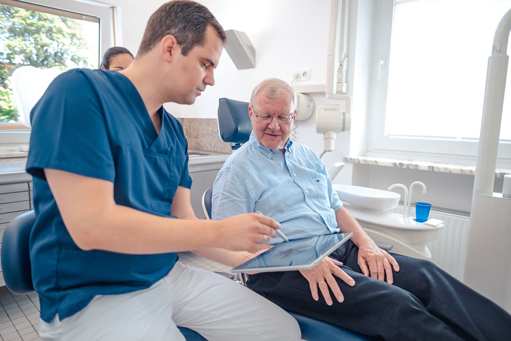 Zahnarzt Giesing - Dr. Koenigsfeld & Kollegen - einfühlsame Erläuterungen der Behandlung für einen älteren Herren auf dem Zahnarztstuhl